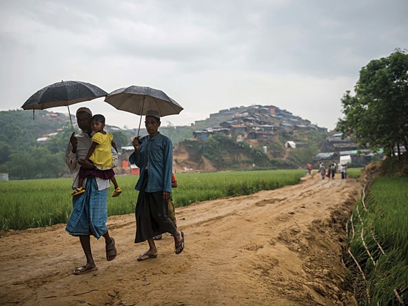 Rohingya Refugees walking with umbrellas holding a toddler